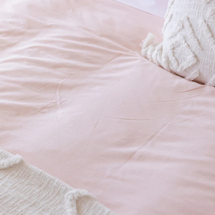Close-up of a soft pink textured blanket with a white pillow and textured fabric corner.