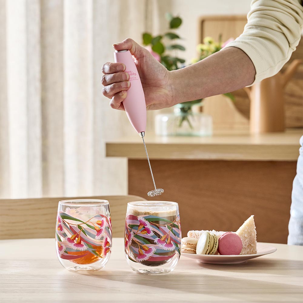 woman holding a milk frother above cup of coffee