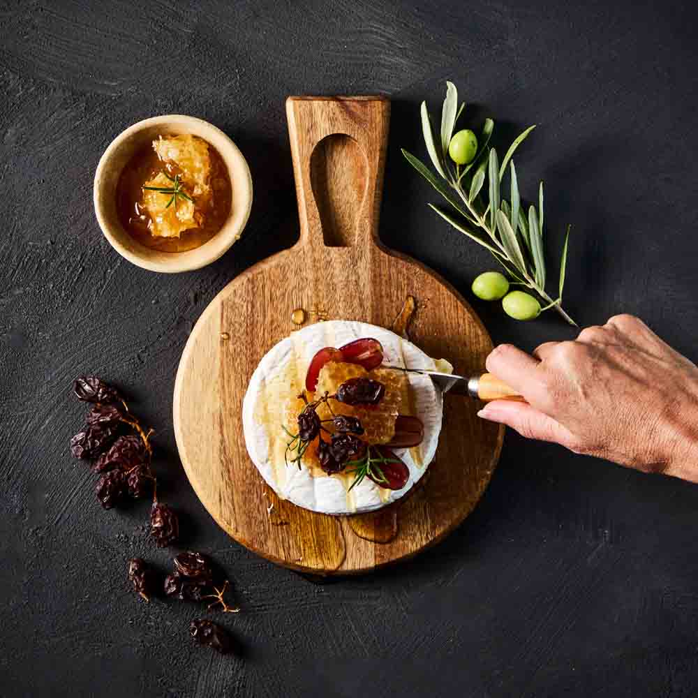 person cutting into brie with cheese knife on cheese board - House