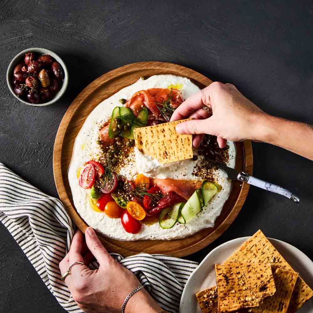person scooping dip with a corn chip from a wooden platter - House