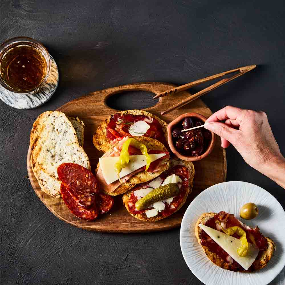person picking an olive from a wooden board with sandwich