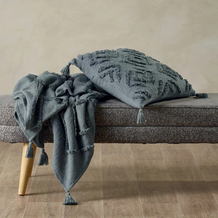 Gray textured throw blanket and pillow on a bench against a beige wall.