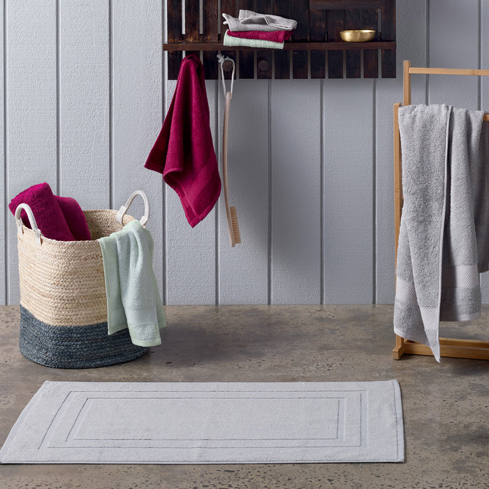 Bathroom scene with towels, a rug, and a basket against a gray wall.
