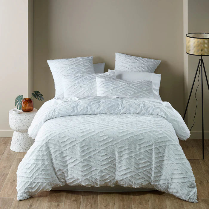Textured white bedding set on a bed in a bedroom with a lamp and plant.
