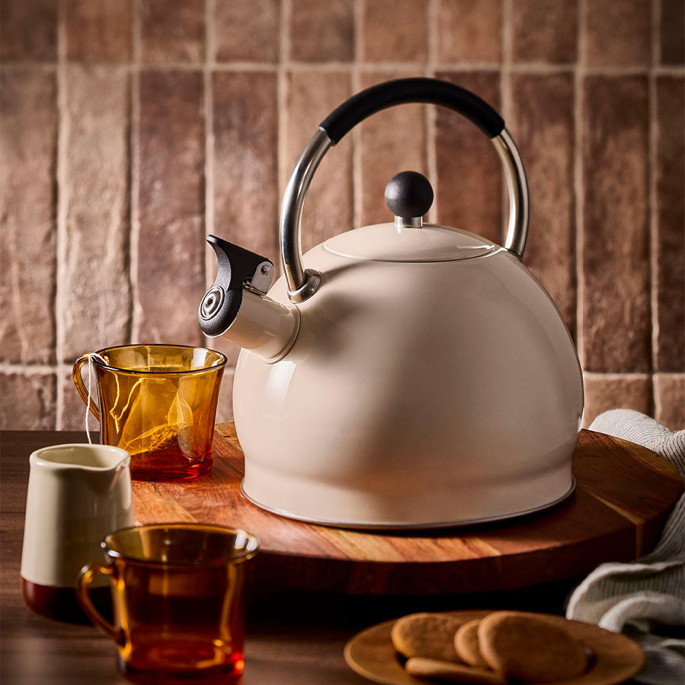 Oat stovetop kettle displayed on a wooden board beside an empty teacup with a tea bag inside.