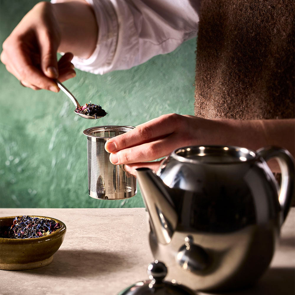 The removable tea strainer is being filled with tea with the tea pot lid off and ready to brew.