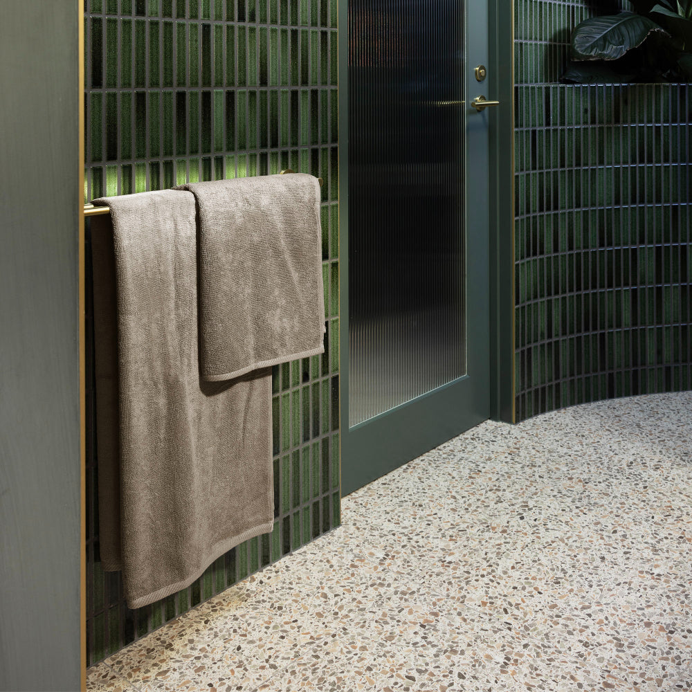 The Bambury bath towel and bath mat in latte hanging in a bathroom on the towel rail.