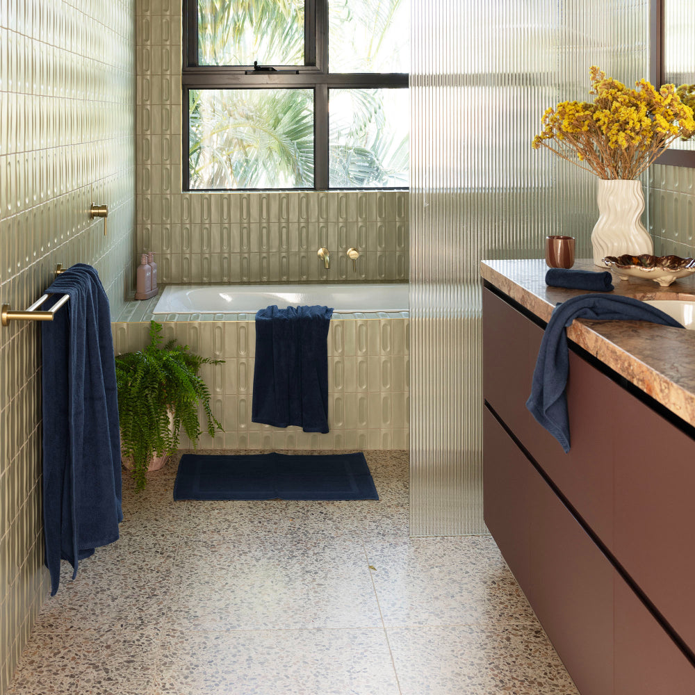 The Bambury Chateau bath mat Navy is layed out on the floor in front of the bath with the rest of the range featuring around the bathroom.
