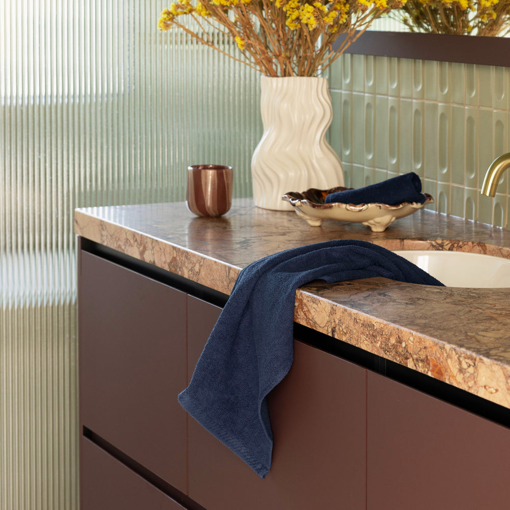 The Bambury Chateau hand towel and face washer in navy displayed on the bathroom vanity ready to use.