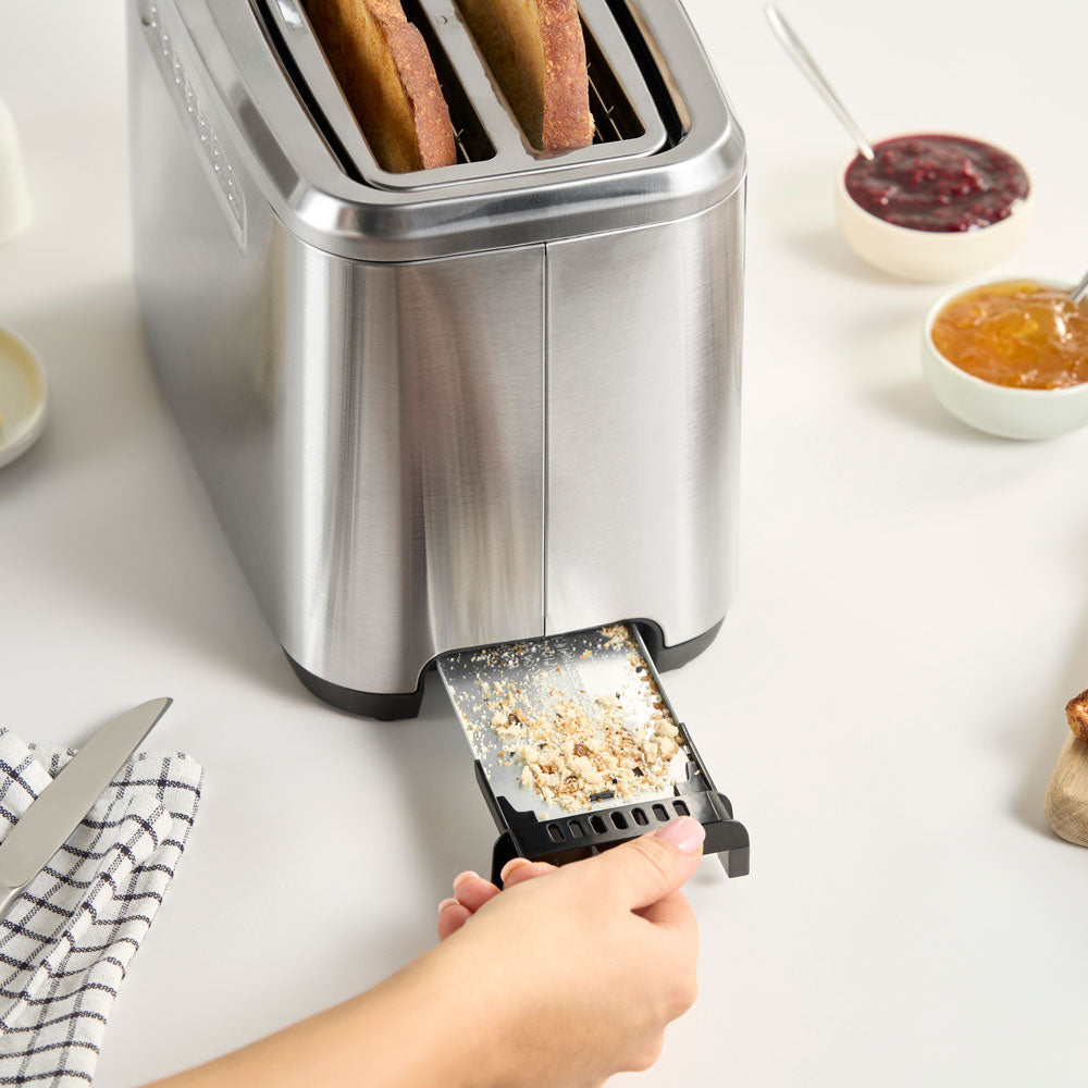 The crumb tray is at the back of the toaster and can be removed by pulling out for convenient cleaning and emptying.
