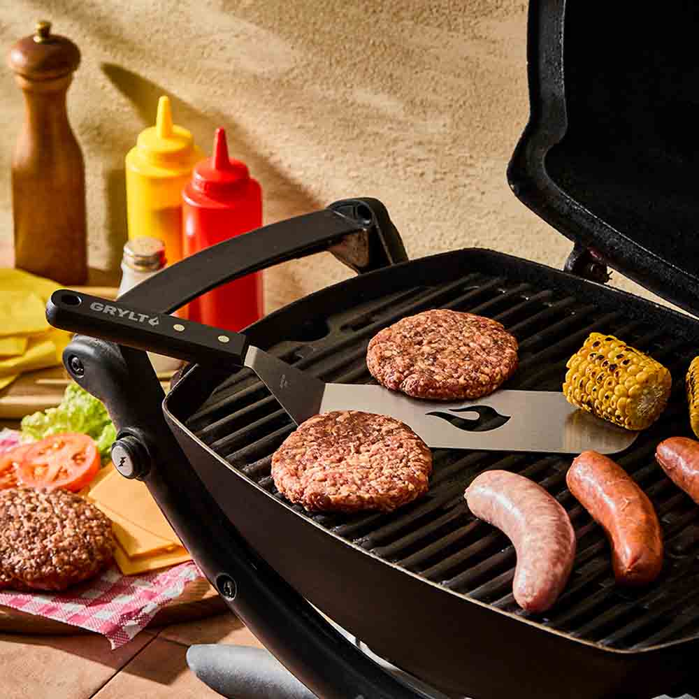 slotted spatula on the BBQ with burgers, corn and sausages- House
