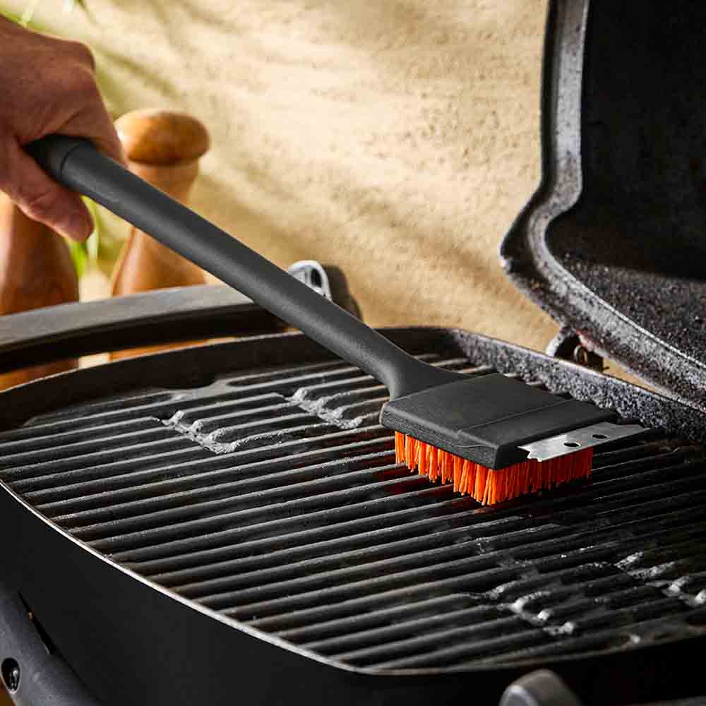 man cleaning BBQ with long handled grill brush - House