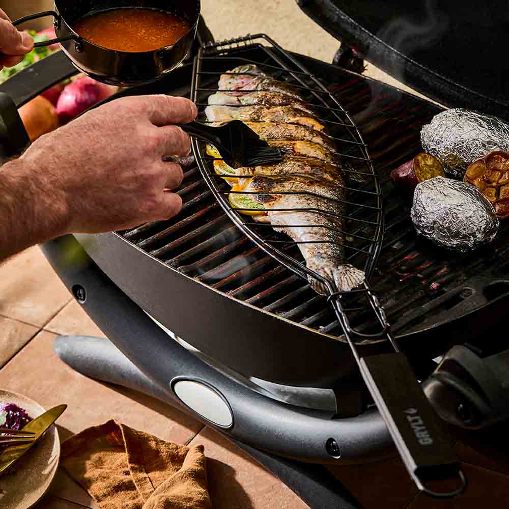 man basting sauce onto a fish on the BBQ - House