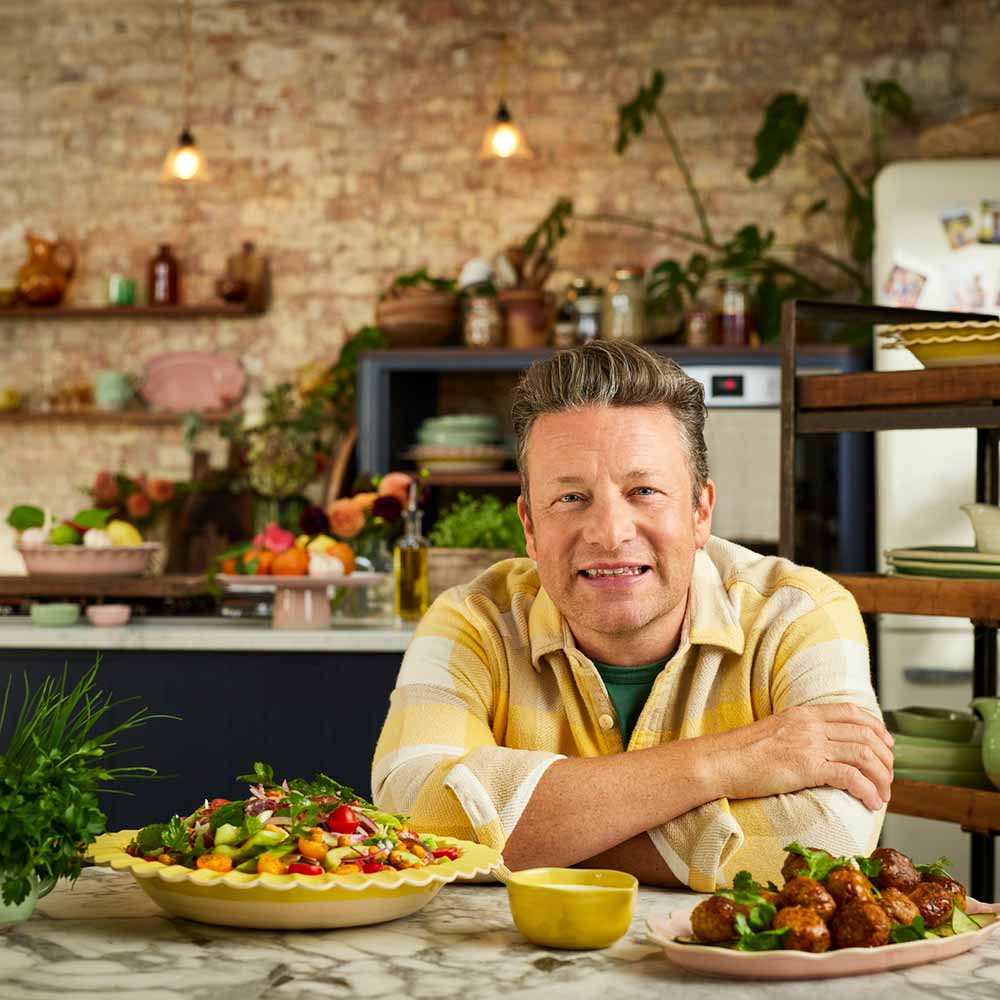Jamie Oliver sitting at table with serving platters full of food - House