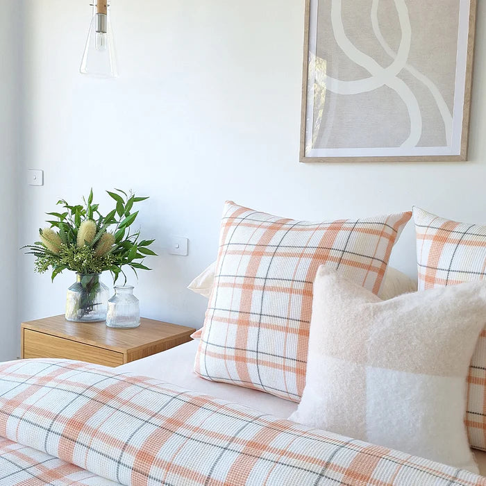 Bedroom with plaid bedding, pillows, and a vase of flowers on a nightstand.