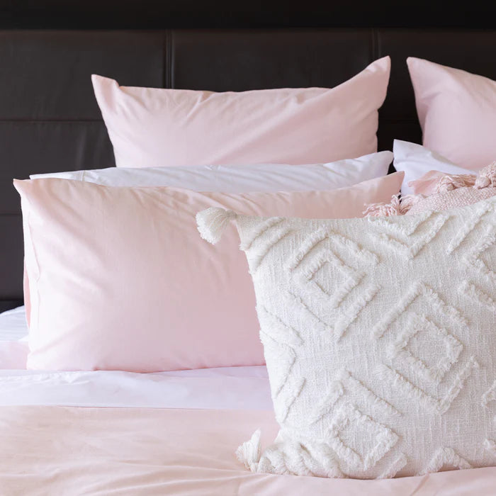 Pink and white textured pillows on a bed with a dark headboard.
