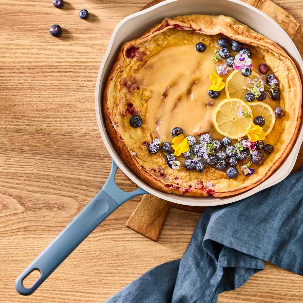 giant pancake dressed with blueberries in a blue frypan
