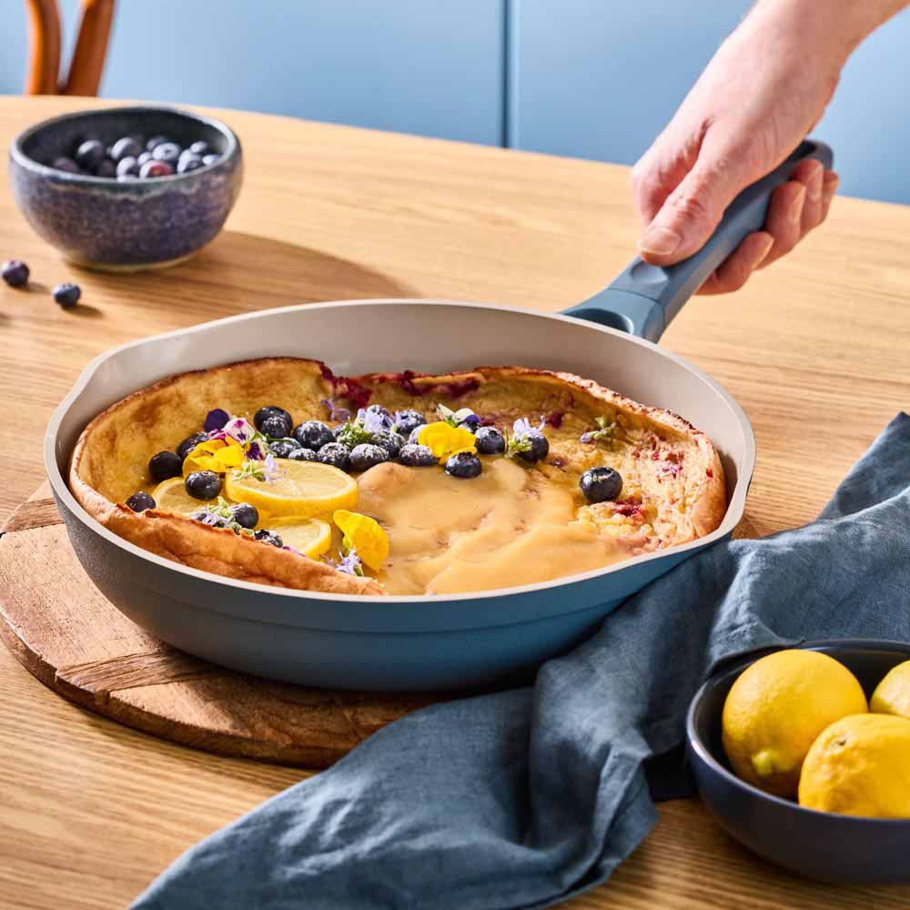 giant pancake dressed with blueberries in a blue frypan