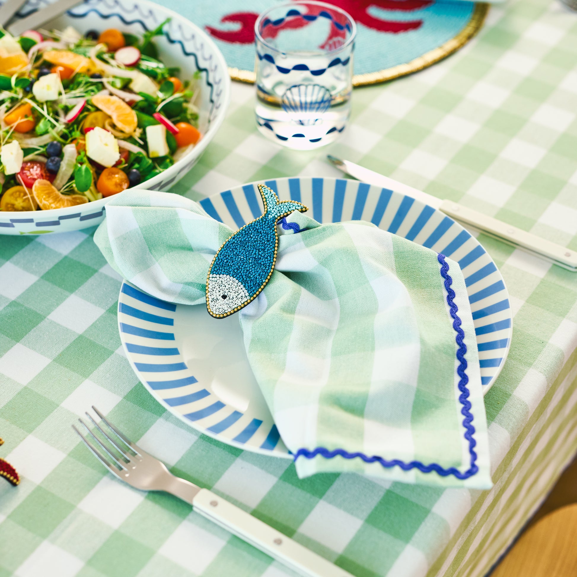 The Porto Gingham sage napkin displayed on a table setting with a fish napkin ring around it.