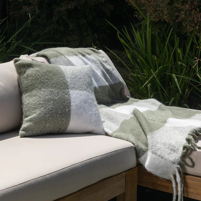 Green and white patterned blanket draped over a cushioned outdoor chair with grass in the background