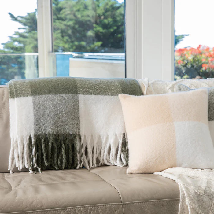 Plaid blanket and pillows on a sofa with a scenic view outside the window.