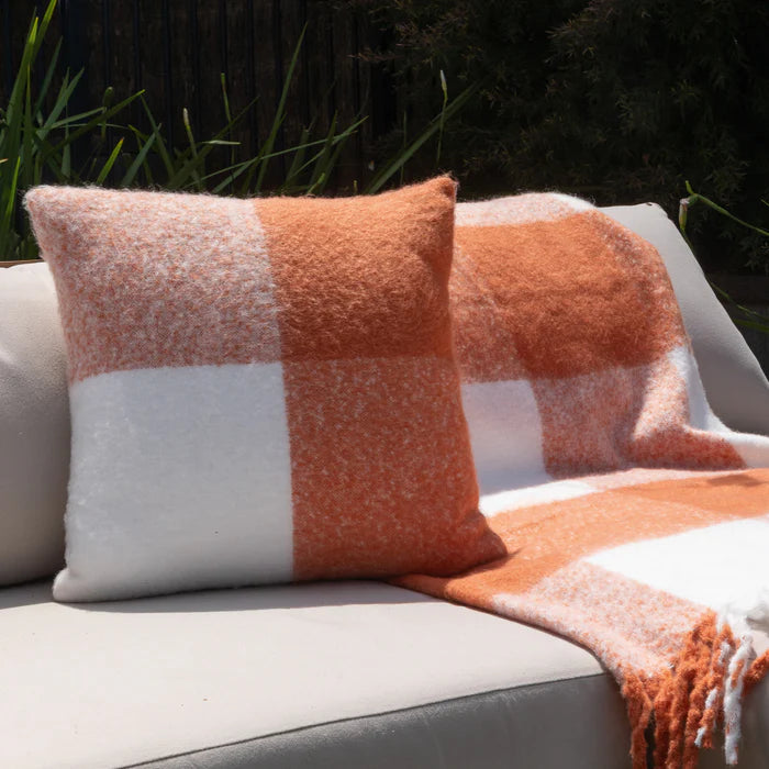 Plaid blanket and pillow on a gray outdoor sofa with greenery in the background