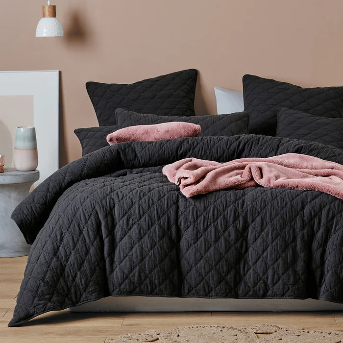 Dark gray quilted comforter with pink blanket and pillows on a bed in a bedroom setting.