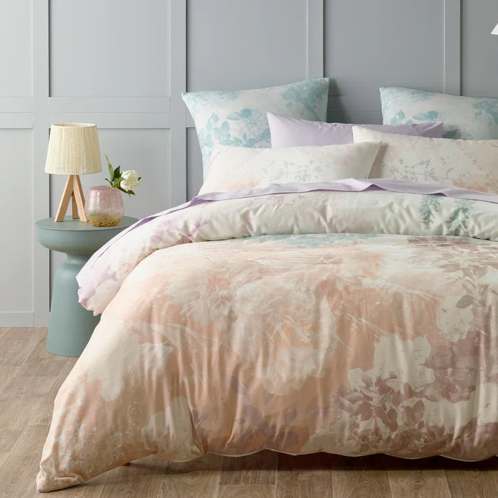 Pastel floral bedding set on a bed with a side table and lamp in a room.