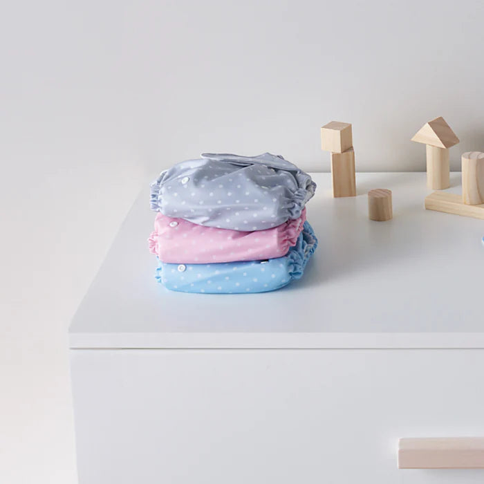 Stack of baby diapers with pink and blue patterns on a white surface with wooden blocks.