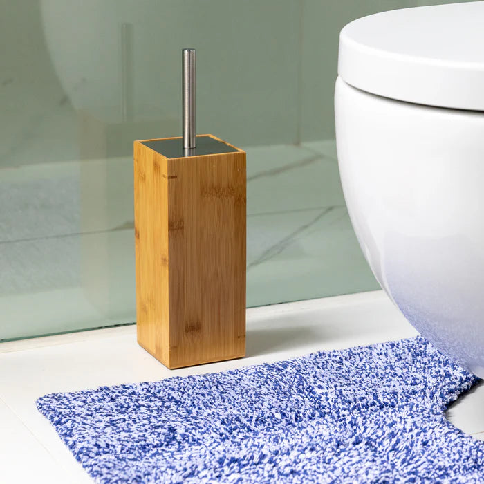 Bamboo toilet brush holder next to a white toilet with a blue bath mat on the floor.