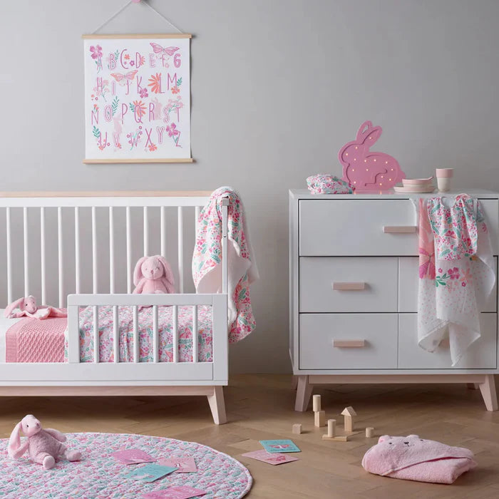 Children's bedroom with crib, dresser, and toys in a pink and white color scheme.
