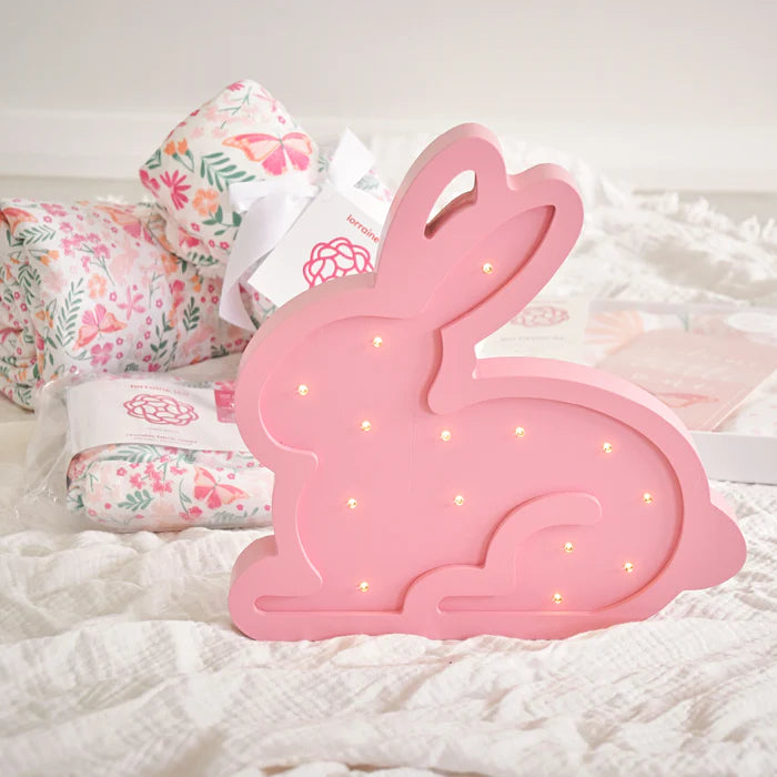 Pink bunny-shaped LED lamp on a white surface with floral-patterned pillows in the background