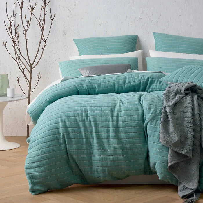 Teal textured comforter set on a bed with pillows and a blanket in a bedroom setting.