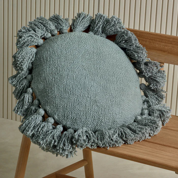 Round cushion with tassels on a wooden chair against a neutral background