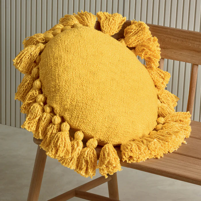 Yellow knitted pillow with tassels on a wooden chair