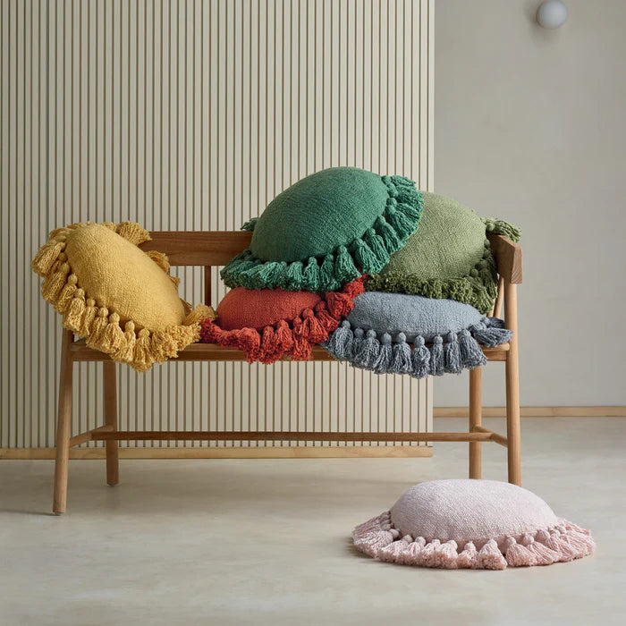 Colorful pillows with tassels on a wooden bench against a neutral wall.