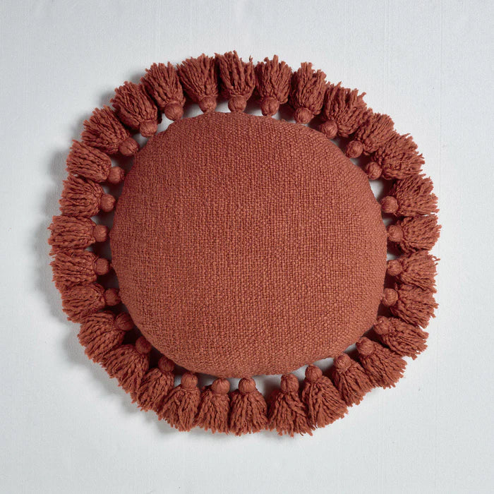 Round brown cushion with tassels on a light gray background