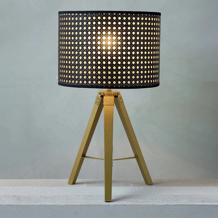 Table lamp with black woven shade and gold metal base on a neutral background