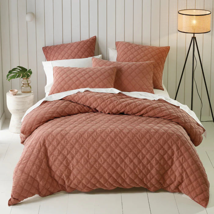 Quilted pink bedding set on a bed with a lamp and plant in the background.