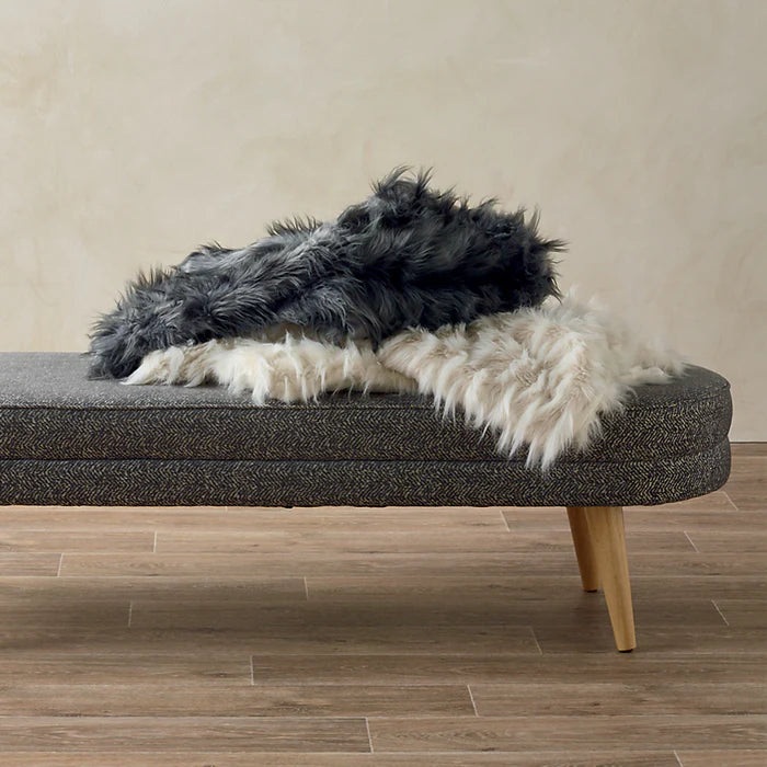 Gray bench with black and white fur throw on a wooden floor.