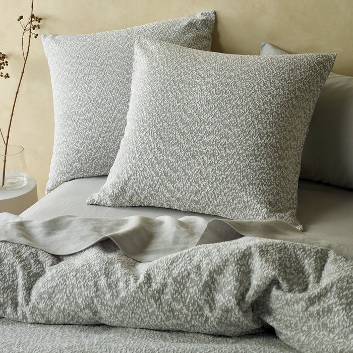 Textured gray pillows and bedding on a bed with a neutral background
