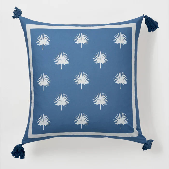 Blue pillow with white palm leaf pattern and tassels on a light gray background