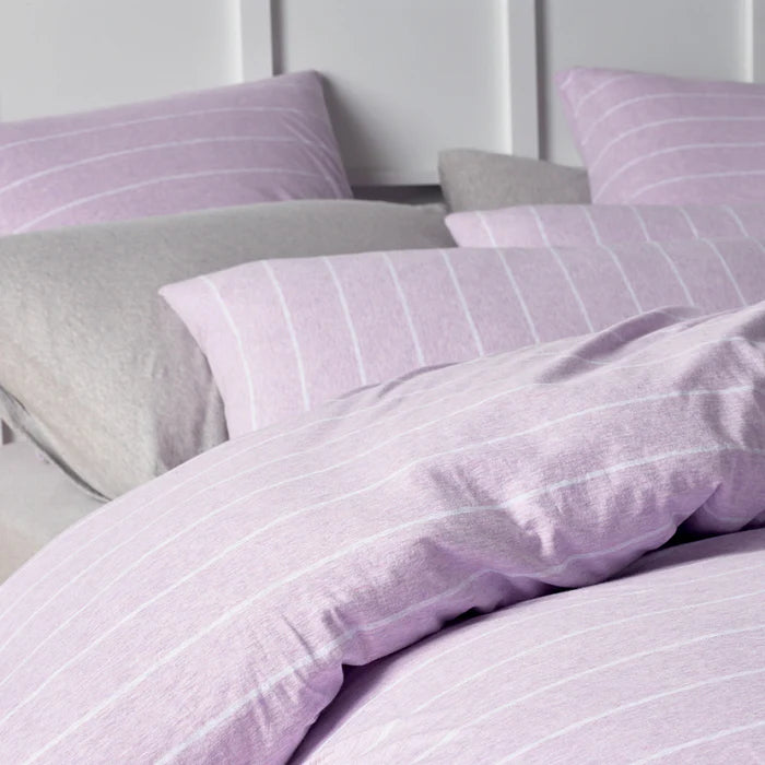 Purple striped bedding set on a bed with pillows.