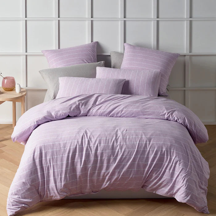 Purple bedding set on a bed with a light gray wall in the background