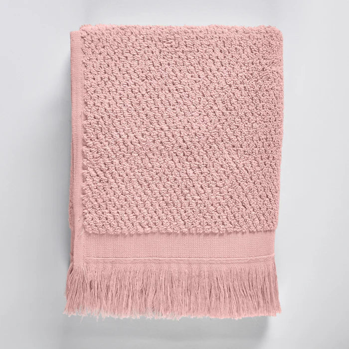 Pink textured bath towel with fringes on a light gray background