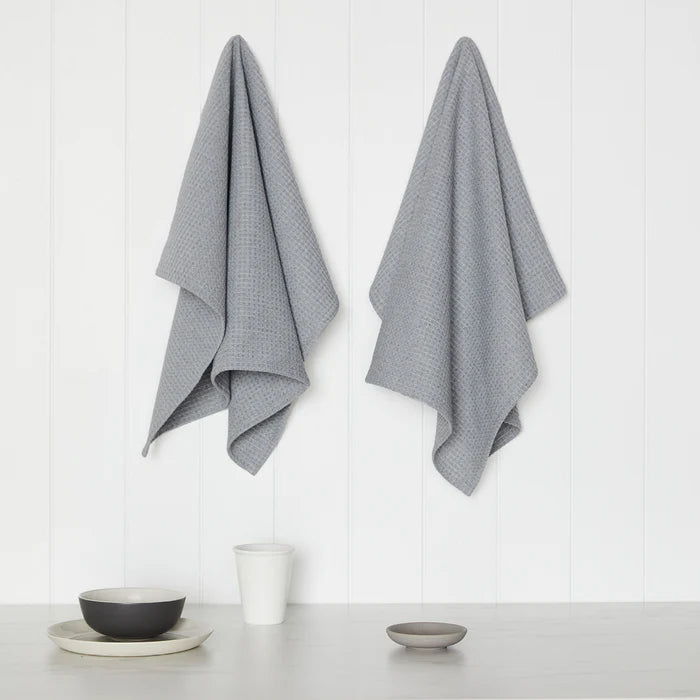 Two gray textured towels hanging on a white wall with minimal decor.