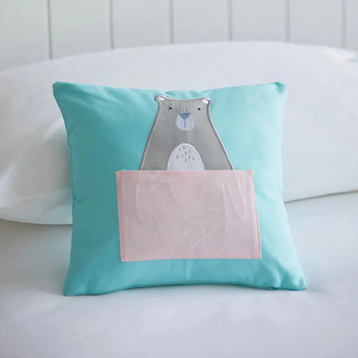 Turquoise pillow with a bear design on a white couch
