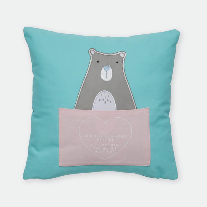 Teal pillow with a bear design and a pink heart pocket on a white background