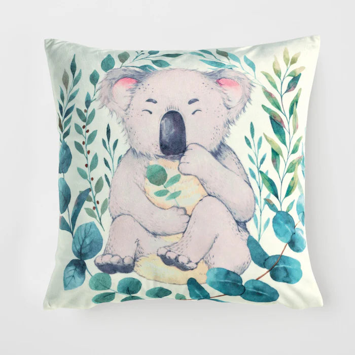 Pillow with a koala holding a leaf surrounded by green leaves on a light background