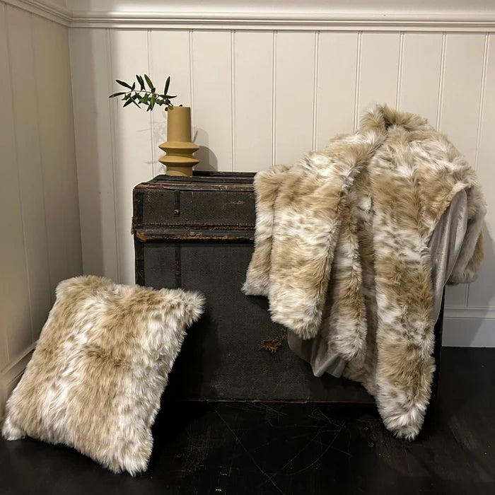 Beige fur throw and pillow on a dark surface against a white paneled wall.